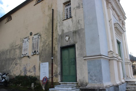 Lapide commemorativa e facciata di un edificio storico a Fontanegli, con segni di usura e vegetazione circostante.