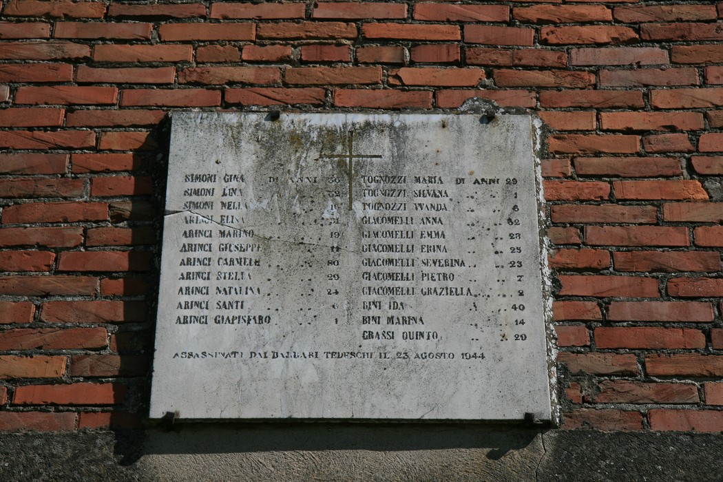Lapide commemorativa della Casa Simoni, con nomi e date di ricordo. Edificio in mattoni rossi.