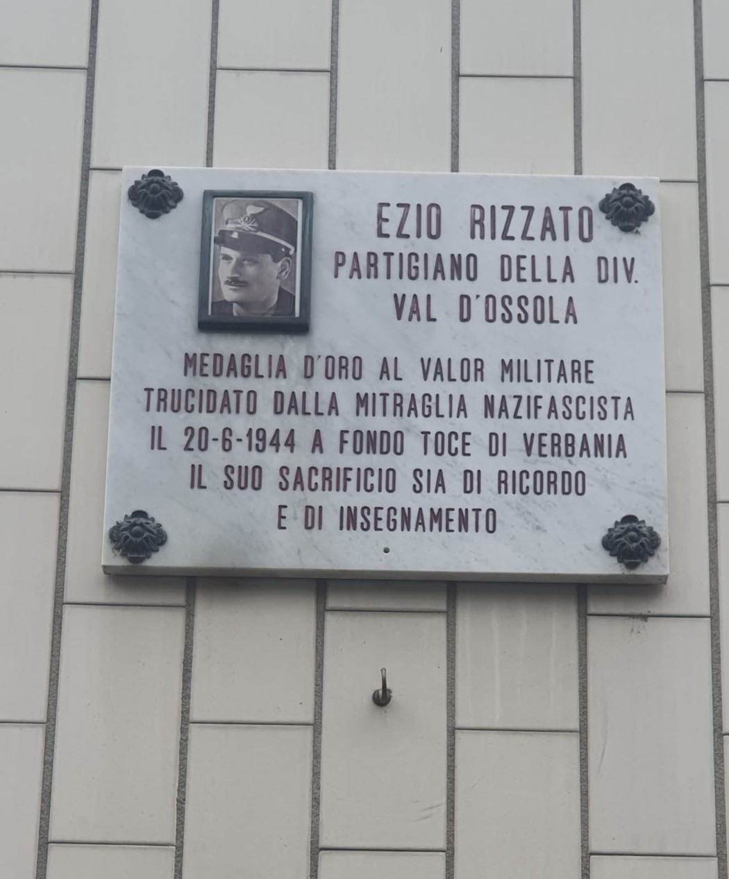 Lapide commemorativa in marmo dedicata a Ezio Rizzato, partigiano della Divisione Val d'Ossola, con foto e dettagli storici.
