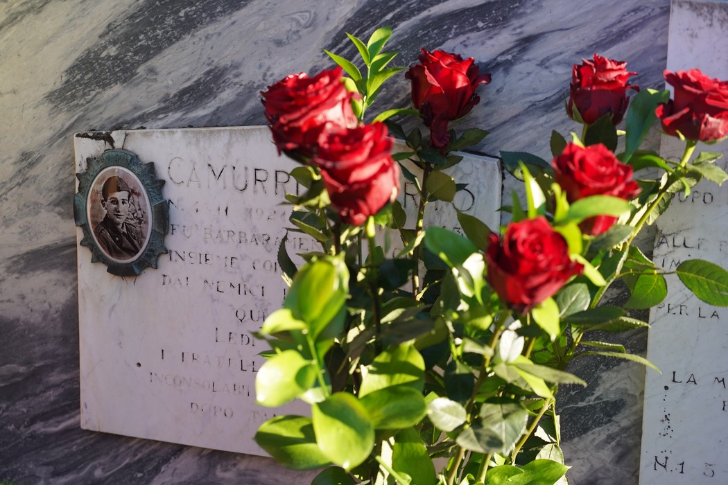Sepolcri con rose rosse in primo piano, sullo sfondo targhe commemorative e decorazioni eleganti.