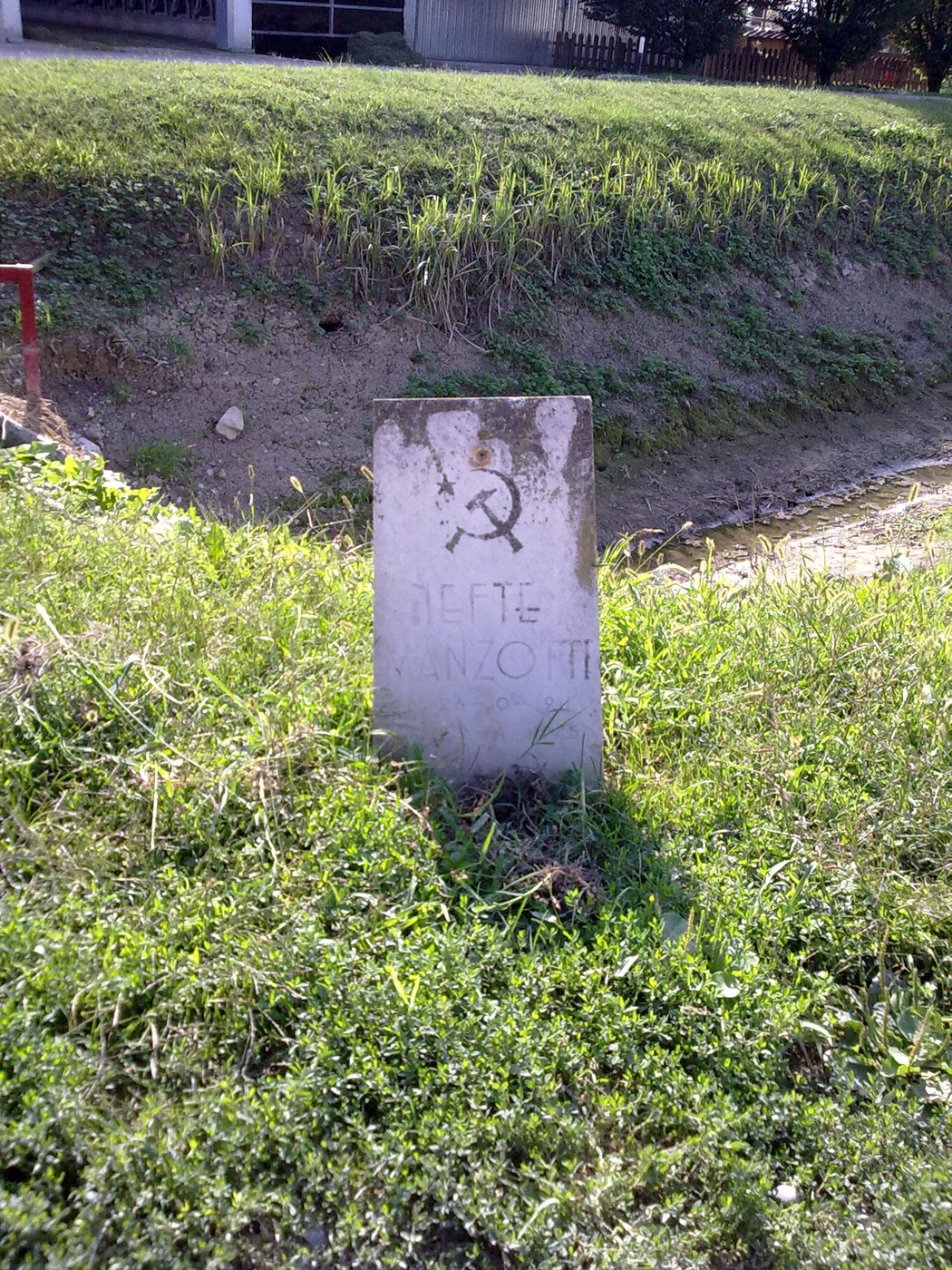 Cippo commemorativo dedicato a Manzotti, situato in un'area verde lungo un corso d'acqua.