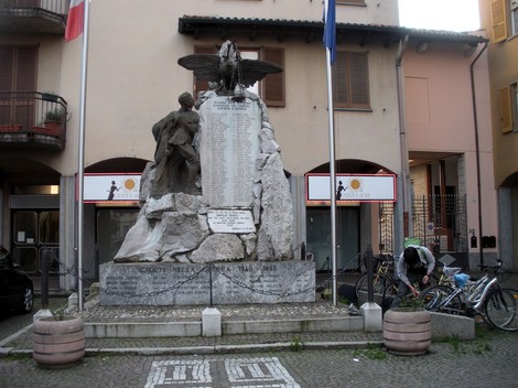Monumento ai caduti di Gropello Cairoli, dedicato alla memoria dei soldati, circondato da bandiere e biciclette.