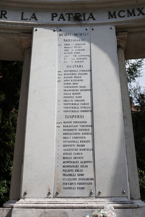Monumento ai Caduti con nomi di partigiani e dispersi inciso su una stele, circondato da vegetazione.
