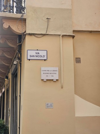 Insegna stradale di Via San Nicolò con una dedica a Masino Meliconi. Murales in un contesto urbano.