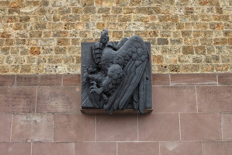 Scultura di un'aquila su muro di pietra, incoronata come simbolo di memoria e onore per la Francia combattente.