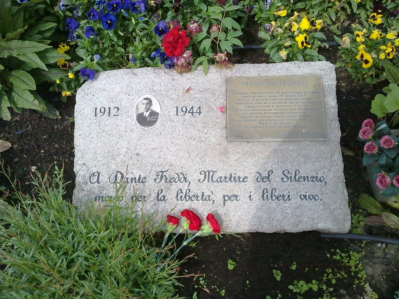 Cippo commemorativo in onore di Dante Freddi, martire per la libertà, adornato da fiori freschi.