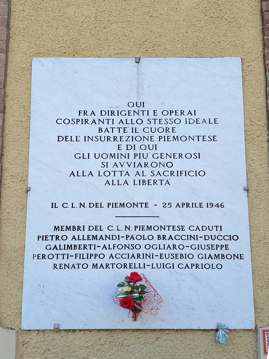 Lapide commemorativa dedicata al Comitato di Liberazione Nazionale piemontese, con fiori rossi e iscrizioni storiche.