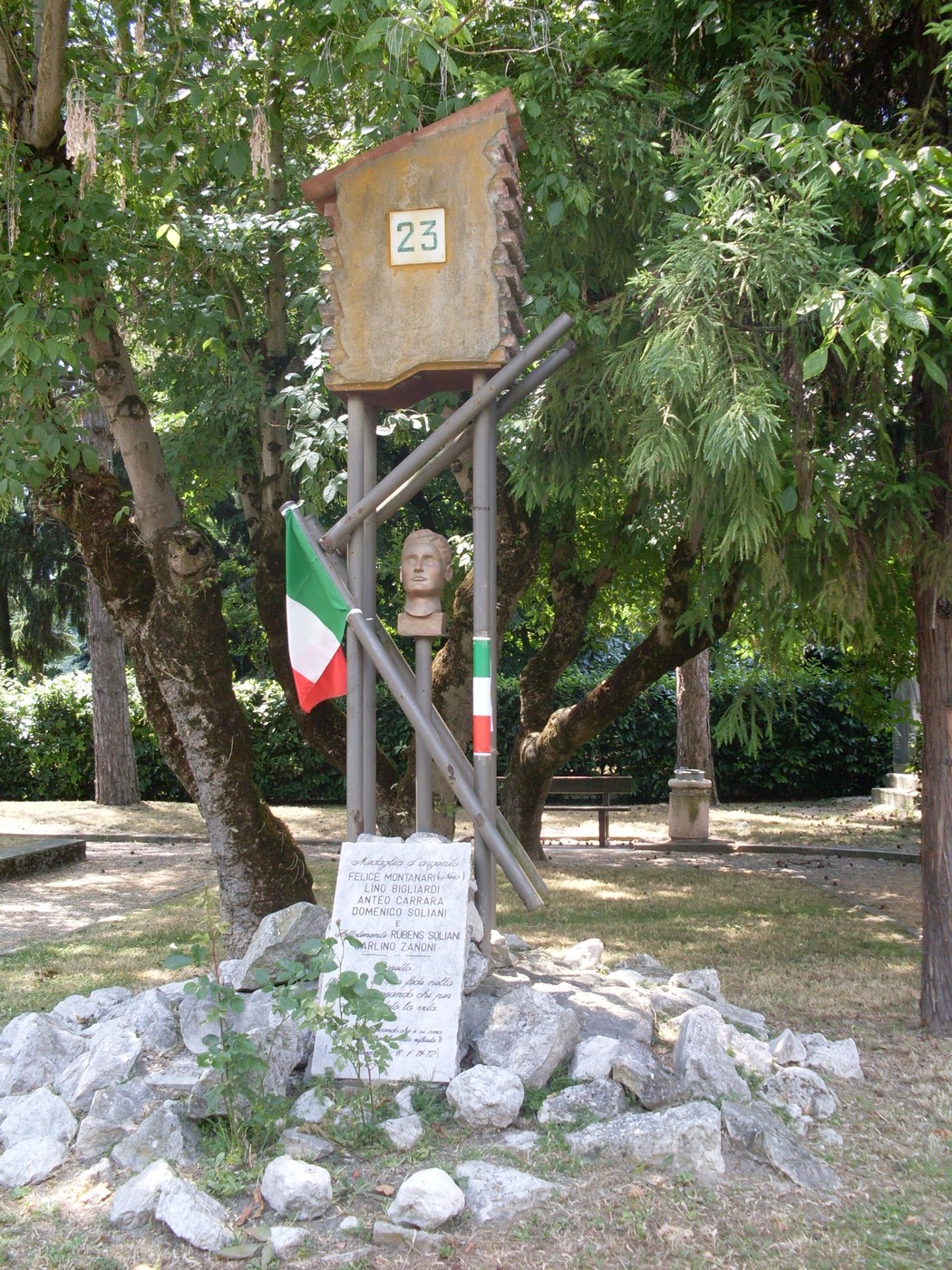 Monumento in onore di Montanari, con scultura e simboli nazionali tra alberi e pietre.