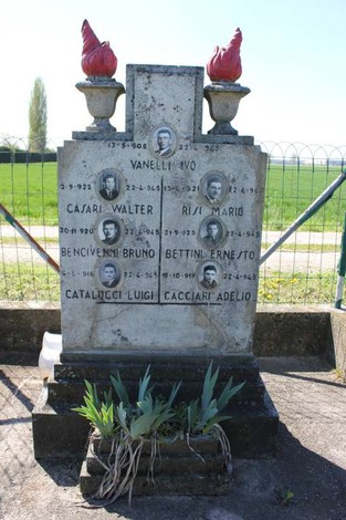 Monumento commemorativo con nomi incisi, dedicato a caduti in guerra, circondato da vegetazione e paesaggio verde.