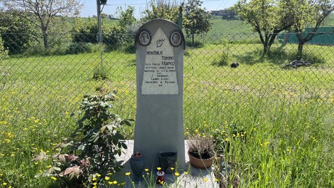 Cippo commemorativo ai Montorsi circondato da erba verde e fiori, con piante ornamentali e un paesaggio tranquillo.
