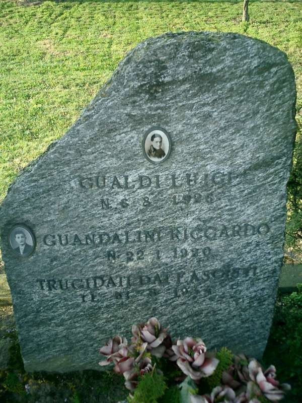 Cippo funerario in pietra con iscrizioni commemorative di Gualdi e Guandalini, circondato da vegetazione.
