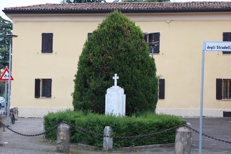 Monumento ai caduti circondato da una vegetazione curata, situato in un contesto urbano.