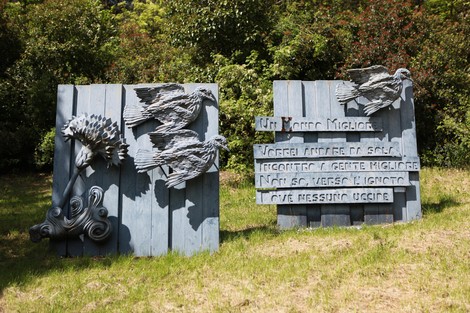 Monumento alle cadute partigiane con bassorilievi e testi commemorativi tra verde e natura.