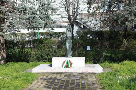 Monumento alla 63° Brigata Garibaldi, con statua e composizione floreale su base marmorea, immerso nel verde.