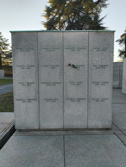 Monumento al "Campo della Gloria" con lastre commemorative e una rosa posata sopra. Atmosfera di riflessione.