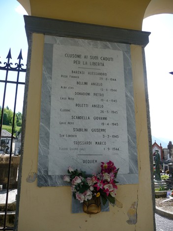 Lapide commemorativa ai caduti partigiani con nomi e date in onore della libertà. Decorata con fiori.