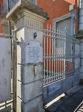 Lapide commemorativa su un cancello ornamentale, con struttura in ferro e pietra. sfondo di un edificio.