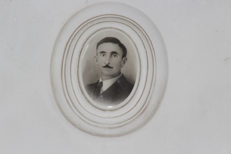 Ritratto in bianco e nero di un uomo con baffi, incorniciato in un ovalino su una superficie bianca.