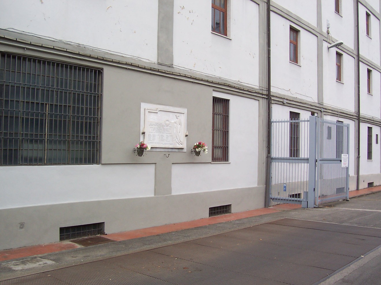 Lapide commemorativa dell'Istituto Farmaceutico Militare su un edificio. Elementi decorativi ai lati.