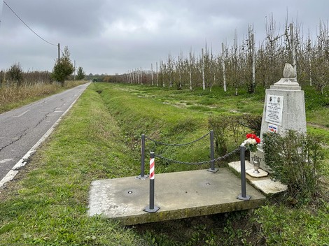 Cippo commemorativo ai Guidetti, immerso in un paesaggio rurale, con fiori e un sentiero a fianco.