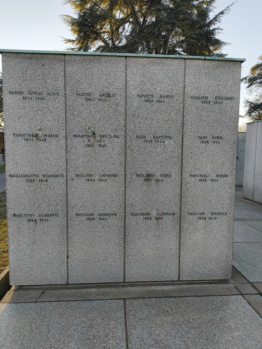 Monumento commemorativo al "Campo della Gloria", con nomi incisi su una parete di pietra. Atmosfera solenne.