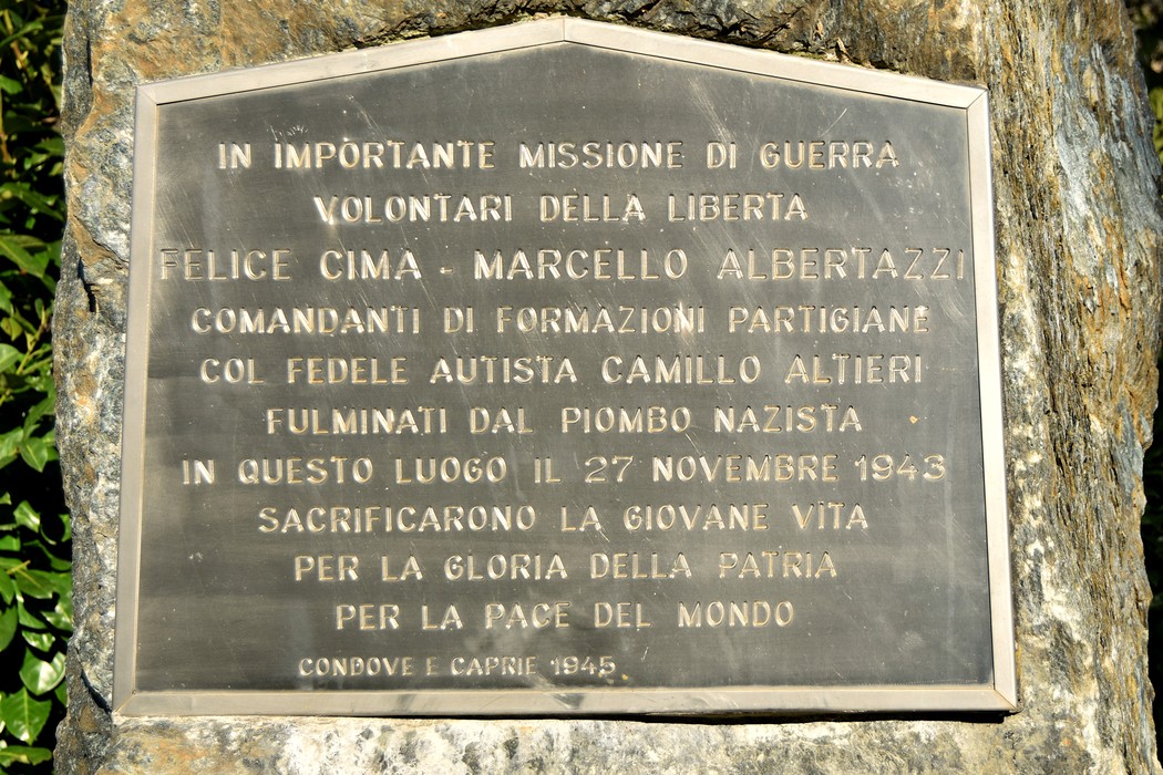 Lapide in bronzo con iscrizione, fissata su una parete rocciosa.