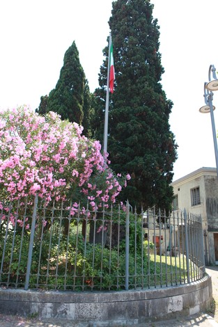 Il Monumento ai caduti del Lido circondato da fiori e alberi, con una bandiera italiana ben visibile.