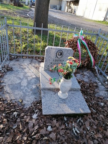 Monumento a Ravaioli, con lapide, fiori e decorazioni, immerso in un contesto naturale.
