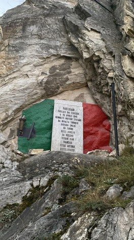 Lapide commemorativa ai partigiani, incastonata in una roccia con il tricolore italiano sullo sfondo.