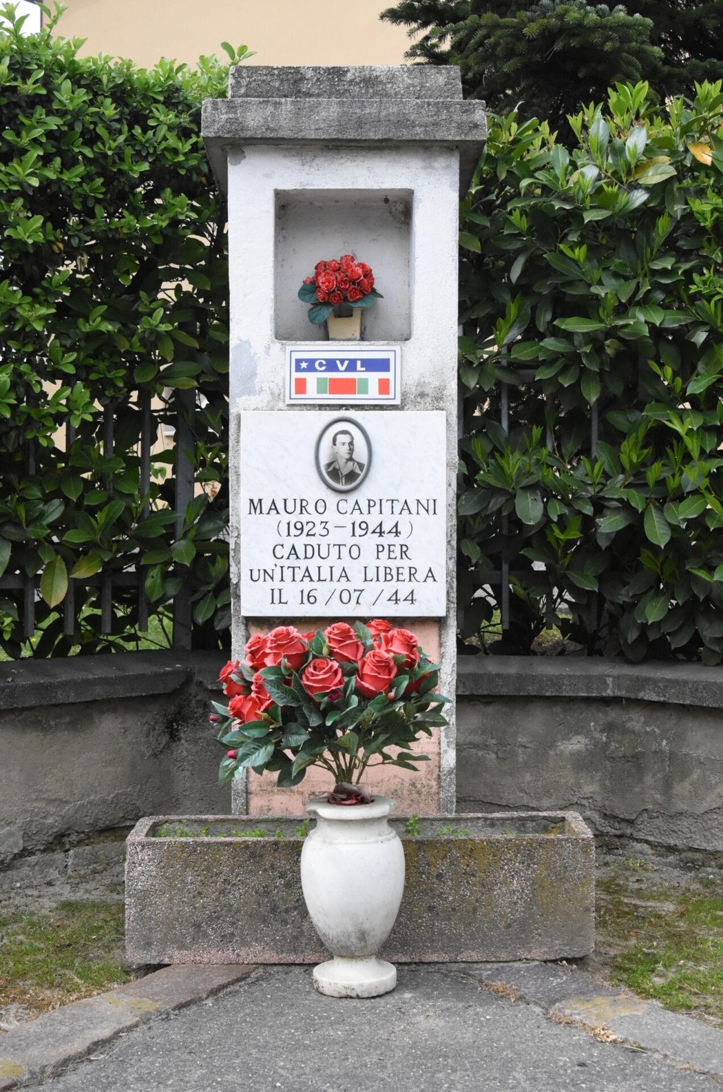 Cippo commemorativo dedicato a Mauro Capitani, caduto per l'Unità d'Italia, con fiori e stemma tricolore.