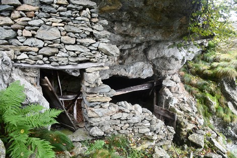 Rifugio partigiano in pietra, immerso nella natura, con vegetazione verdeggiante e rocce circostanti.