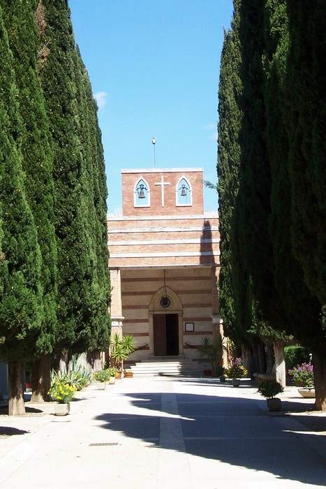 Cappella dei caduti, immersa nella natura, con cipressi che la circondano, simbolo di memoria e rispetto.