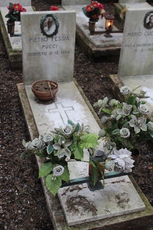 Tombe decorate con fiori e candele, dedicate ai caduti per la Libertà, in un ambiente di rispetto e commemorazione.