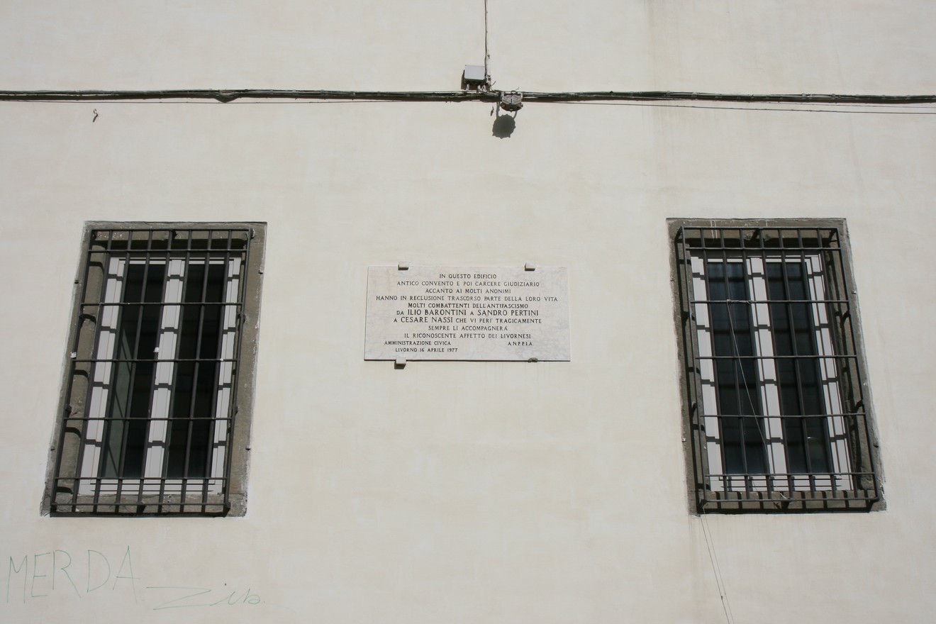 Lapide commemorativa sul carcere giudiziario, con finestre con grate e muro bianco.