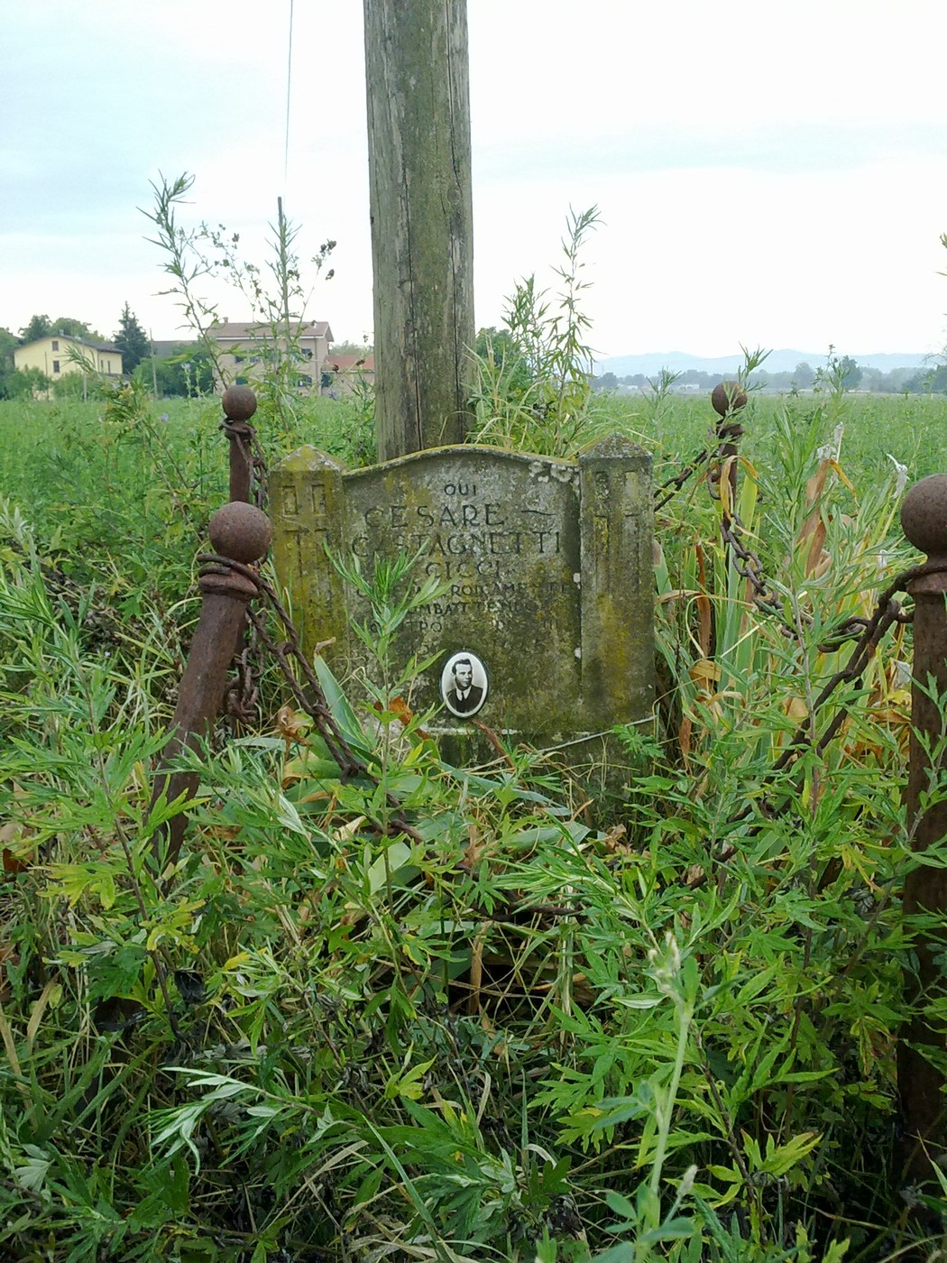 Cippo commemorativo a Castagnetti, circondato da vegetazione e recintato da una vecchia ringhiera.
