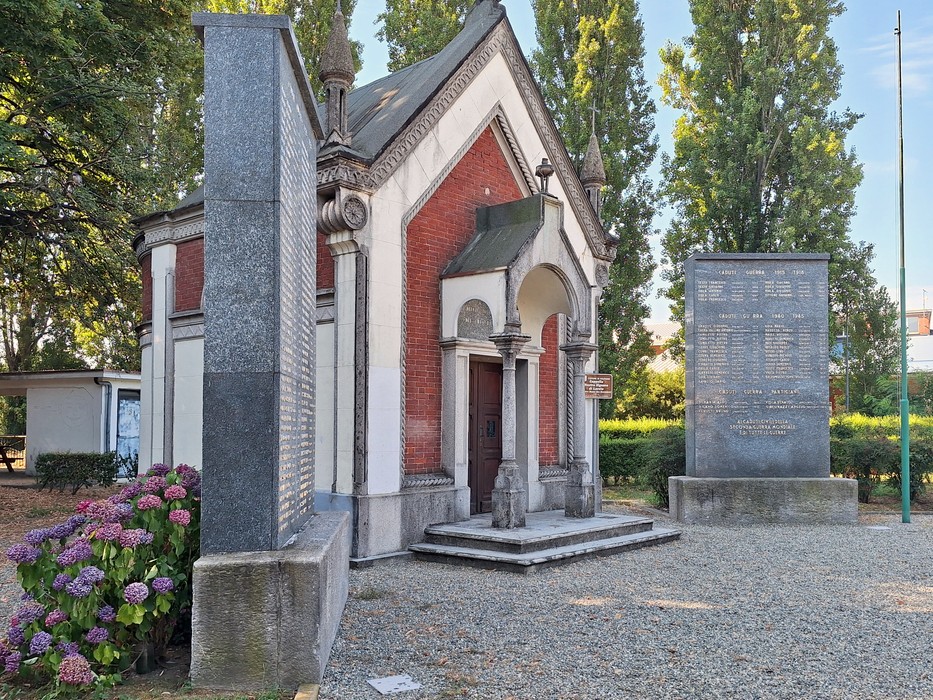 Monumento ai caduti, un edificio commemorativo con dettagli architettonici e aiuole fiorite sullo sfondo.