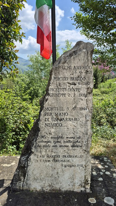 Monumento ai fucilati di Villa Spada, commemorazione con pietra tombale e bandiera tricolore sullo sfondo.