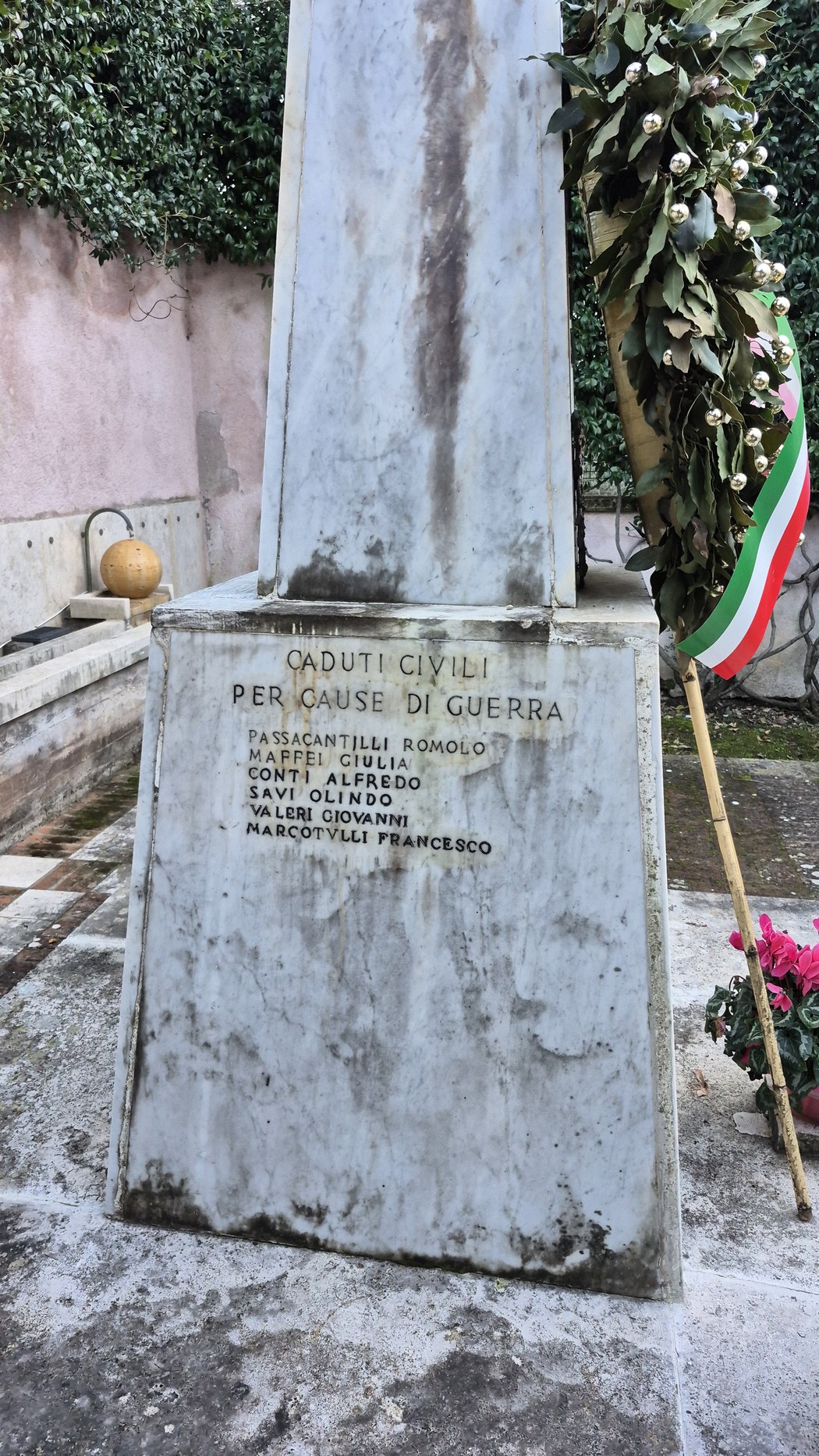Monumento ai caduti, in marmo, decorato con corone e bandiera tricolore, commemorazione di vittime di guerra.