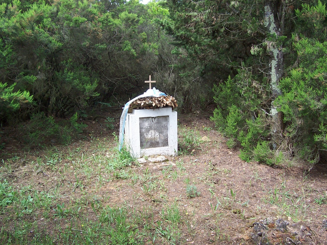 Cippo in un'area boschiva, con una croce e decorazioni naturali, simbolo di ricordo e commemorazione.