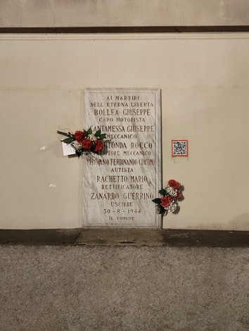 Lapide commemorativa dedicata ai martiri della libertà, con nomi e fiori.