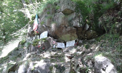 Lapidi commemorative sull'Alpe Morcei, circondate da vegetazione e un tricolore italiano.