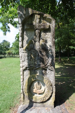 Monumento ai caduti, con croce e simboli di libertà, immerso nel verde di un parco.