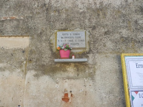 Lapide commemorativa con fiori, affissa su un muro di pietra, in ricordo di un evento importante.