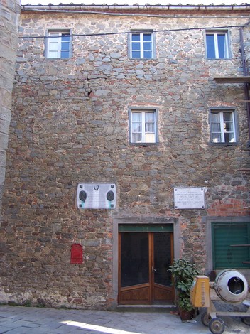Lapide commemorativa su una facciata di edificio in pietra, con dettagli architettonici tipici.