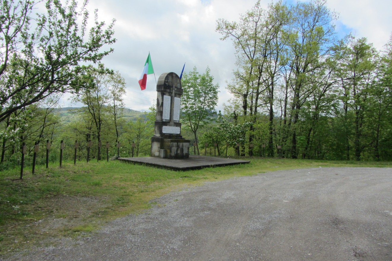 Monumento ai martiri dei Boschi di Ciano immerso nella natura, con bandiere e un panorama verdeggiante.
