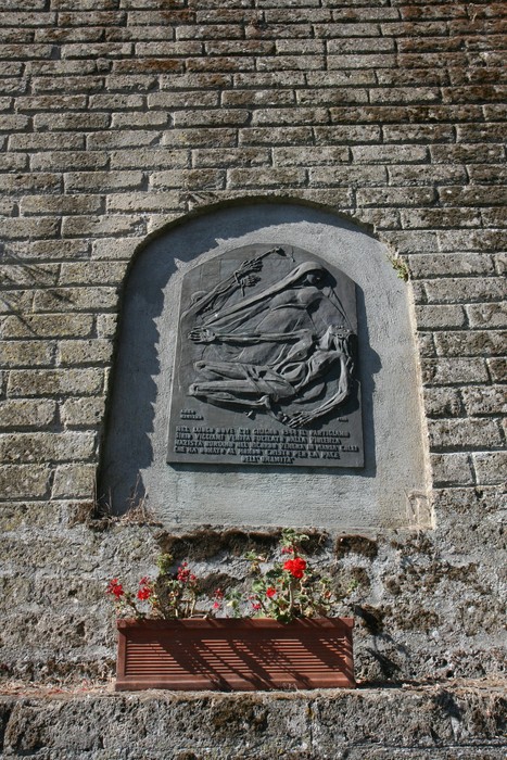 Lapide di Buriano, commemorativa, posta su un muro di pietra con fiori sotto. Rappresenta la memoria storica locale.
