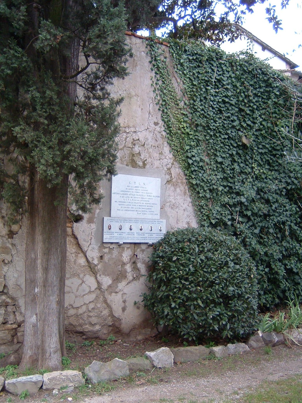Lapide commemorativa dedicata ai fucilati di Villa Dani, immersa nella vegetazione.