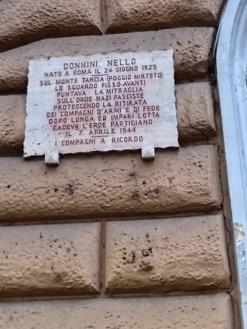 Lapide commemorativa dedicata a Nello Donnini, situata su un muro, con testo di omaggio e data commemorativa.