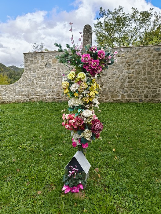 Cimitero di Casaglia: lapide decorata con fiori artificiali in un ambiente naturale e sereno.