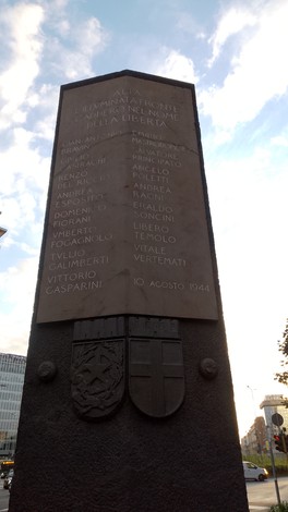 Monumento ai martiri di Piazzale Loreto, commemorazione con nomi su rilievo e stemmi, cielo blu sullo sfondo.